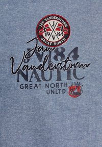 Helles blaues Gewebe mit gesticktem Logo im kreisförmigen Design, Text in Marineblau und Schwarz sowie roten Akzenten. Bemerkenswerte Nähdetails sichtbar.