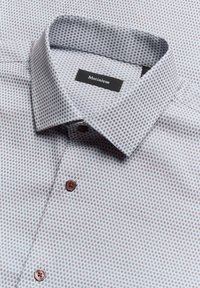 Korte mouw shirt in lichtgrijze katoen met een klein herhalend patroon in rood en blauw. Inclusief button-down kraag en bruine knopen.