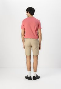 Pink short-sleeve t-shirt paired with khaki shorts. Black sneakers with white socks. Simple design, casual fit, no visible logos or patterns.