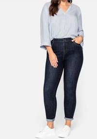 Jeans ajustados azul oscuro con una textura desgastada y puños enrollados, combinados con una blusa de rayas azul claro y zapatillas blancas.