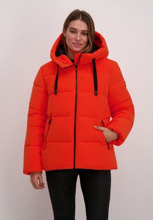 Oranje pufferjack met een capuchon, voorzien van een ritssluitingen aan de voorkant, zwarte accenten en zijzakken. De stof is soepel met een gewatteerd patroon.