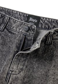 Zwarte denim jeans met een vervaagde textuur, ritsluiting en knoopsluiting. Kenmerkt een label met de tekst "Utopja" en maat "XS."