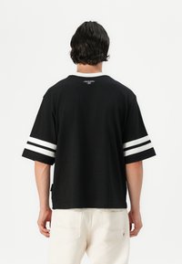Sort kortærmet t-shirt med hvide striber på ærmerne. Materialet virker glat og har en afslappet pasform. Enkelt bagstykke med minimal branding ved halsen.