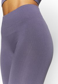 Leggings viola a coste con vita alta e design aderente, che evidenziano una texture morbida e elastica.