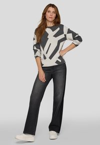 Grau-weiß gemusterter Pullover mit geometrischem Design, kombiniert mit weit geschnittenen schwarzen Jeans und weißen Sneakers. Lässiger Look.