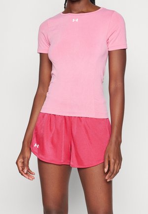 Persoon die een roze atletisch shirt met korte mouwen draagt en rode atletische shorts met witte logo's op beide kledingstukken.