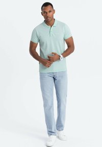 Minttuvihreä polo-paita, jossa on pehmeä rakenne, lyhyet hihat ja kaulus, yhdistettynä vaaleansinsisiin farkkuihin ja valkoisiin lenkkareihin.