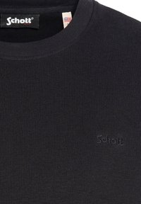 Chemise noire à manches longues côtelée avec un col rond. Présente une broderie discrète de la marque et une étiquette avec un drapeau américain. Texture douce.