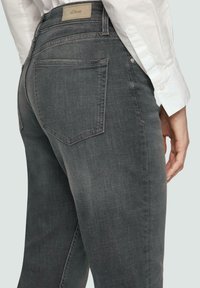 Jeans en denim gris foncé avec un design épuré, des coutures discrètes, deux poches arrière avec une couture en empiècement et une étiquette de marque à la taille.