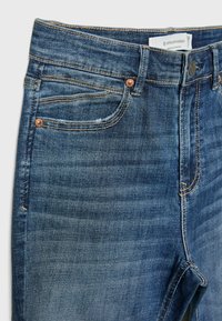 Tummansiniset farkut keskipestynä, joissa on klassinen viiden taskun muotoilu, kupariset niitit ja kontrastiväristä ompelua saumoissa.