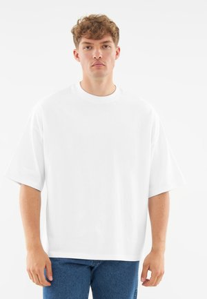 Hvid oversized t-shirt med rund halsudskæring og korte ærmer, lavet af blødt stof, parret med blå denim jeans.
