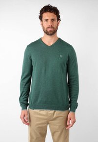 Pull vert en V en tissu texturé. Doté de manches longues et de poignets et ourlet côtelés. Petit logo sur la poitrine.