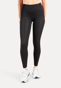 Zwarte leggings met hoge taille gemaakt van glad, rekbaar materiaal. Heeft een aansluitend design en een logodetail op de tailleband. Gecombineerd met witte sneakers.