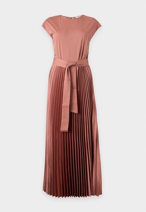 Femme aux longs cheveux foncés portant une robe midi plissée rose poudrée à manches courtes et ceinture à la taille, associée à des escarpins beiges.