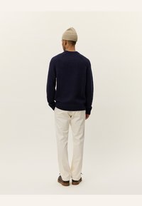 Navy blue knitted sweater with ribbed cuffs and hem, paired with cream-colored pants and a beige beanie, viewed from the back.