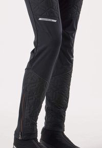 Pantaloni neri con texture trapuntata sulla parte inferiore delle gambe, dotati di tasche con cerniera e impreziositi da una patch con logo sul lato e una cerniera ai polsini.