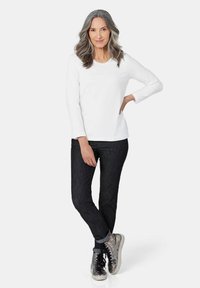 Weißes Langarmhemd, kombiniert mit dunklen Jeans und metallischen High-Top-Sneakern. Einfaches Design mit lockerer Passform.