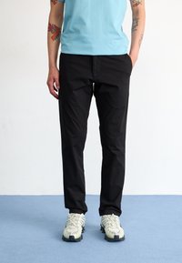Black, lightweight trousers with a straight cut, paired with a light blue shirt and white sneakers featuring textured details.