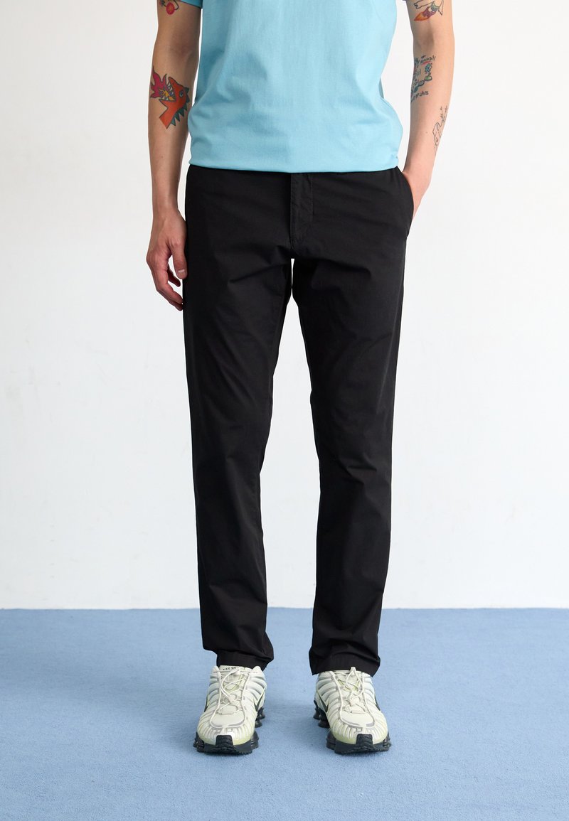 Black, lightweight trousers with a straight cut, paired with a light blue shirt and white sneakers featuring textured details.