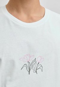 Bílý bavlněný tričko s grafikou dvou obrysových růžových tulipánů se zelenými listy, kulatým výstřihem a krátkými rukávy.