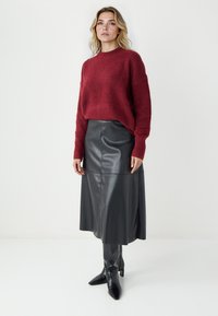 Bordeaux gebreide trui met lange mouwen, gecombineerd met een zwarte leren midi-skirt. Glanzende leren kniehoge laarzen met spitse neuzen.