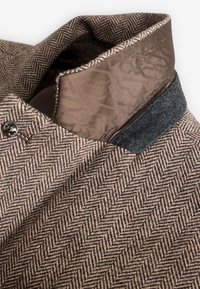 Col de manteau en laine marron à motif chevron avec doublure intérieure en satin marron et sous-col en feutre gris foncé, fermé par un bouton-pression en métal.