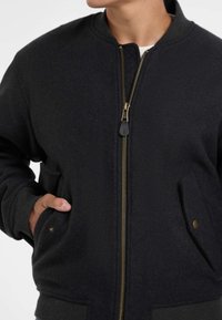 Giubbotto bomber nero realizzato in tessuto misto lana, con zip frontale, polsini a coste e tasche laterali con dettagli dorati.
