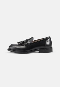 Zwarte gepatineerde leren loafers met een ronde neus, decoratieve kwastjes, gegraveerde details en een lage gestapelde hak. Glad, glanzend oppervlak.