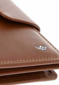 Coin de portefeuille en cuir marron avec couture détaillée et petit logo argenté en forme de feuille sur une surface lisse.