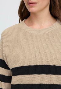 Maglione beige a maglia con ampie strisce nere, caratterizzato da un colletto a girocollo ribattuto e tessuto testurizzato. Si concentra su un fit casual e rilassato.