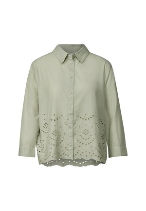 Camisa de botón verde claro con mangas largas; presenta patrones recortados a lo largo del dobladillo y el yugo para aportar textura y detalle de diseño.