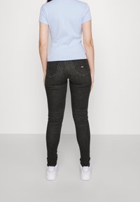 Tunna svarta denimjeans med hög midja, förstärkta sömmar och bakfickor, kombinerat med en ljusblå figursydd T-shirt och vita sneakers.