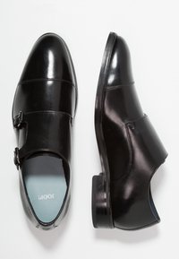 Zwarte leren dresschoenen met een ronde neus, enkele gespsluiting en een gladde afwerking. Beschikt over een blauwe binnenzool en een platte hak.