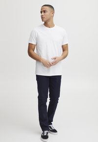 Camiseta de algodón blanca, de manga corta, con cuello redondo, combinada con jeans de color azul oscuro y zapatillas negras. Diseño simple con un ajuste clásico.