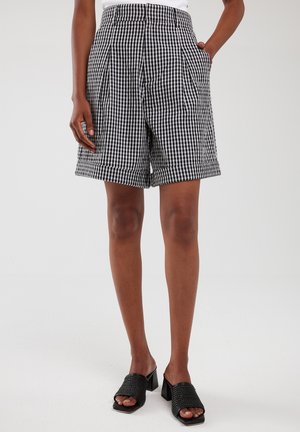 Schwarz-weiße Shorts im Gingham-Muster mit hoher Taille, Falten, Seitentaschen und umgeschlagenen Säumen, kombiniert mit schwarzen offenen Mules.