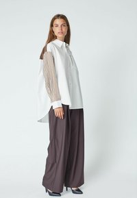 Camicia bianca con maniche a strisce marroni, dettaglio della tasca frontale. Abbinata a pantaloni marroni a gamba larga e tacchi neri. Design semplice e strutturato.