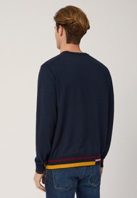 Sweatshirt blu navy con collo rotondo, maniche lunghe e orlo rigato multicolore in rosso, giallo e marrone. Tessuto morbido.