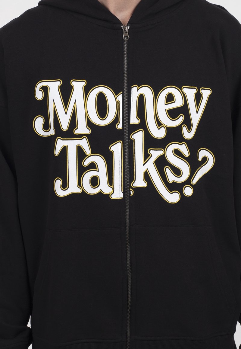 Sweat à capuche noir zippé avec un grand texte blanc et jaune sur le devant disant "Money Talks ?". Matière douce avec une texture lisse.
