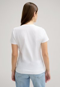 Witte katoenen t-shirt met korte mouwen en een ronde hals. Zachte textuur, iets getailleerde pasvorm en een schoon, eenvoudig ontwerp.