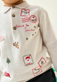 Crème trui met kleine bruine knopen. Bevat kleurrijke geborduurde details, waaronder een sneeuwman, rendier en feestelijke stempels.