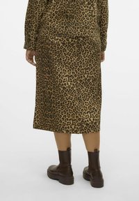 Leopardenmuster Rock aus weichem Stoff, knielang, mit geradem Schnitt. Getragen mit braunen Ankle Boots, die eine strukturierte Oberfläche zeigen.
