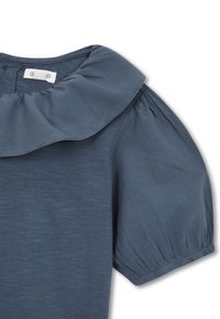 Mörkblå topp med volangkrage och puffärmar. Mjuk textur med subtila tygvariationer. Knäpps med två knappar bak.