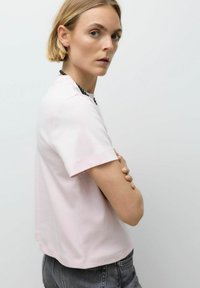 Roze katoenen T-shirt met korte mouwen, relaxte pasvorm, gebogen zoom en een ronde halslijn. Model draagt een donkergrijze spijkerbroek met minimale accessoires.