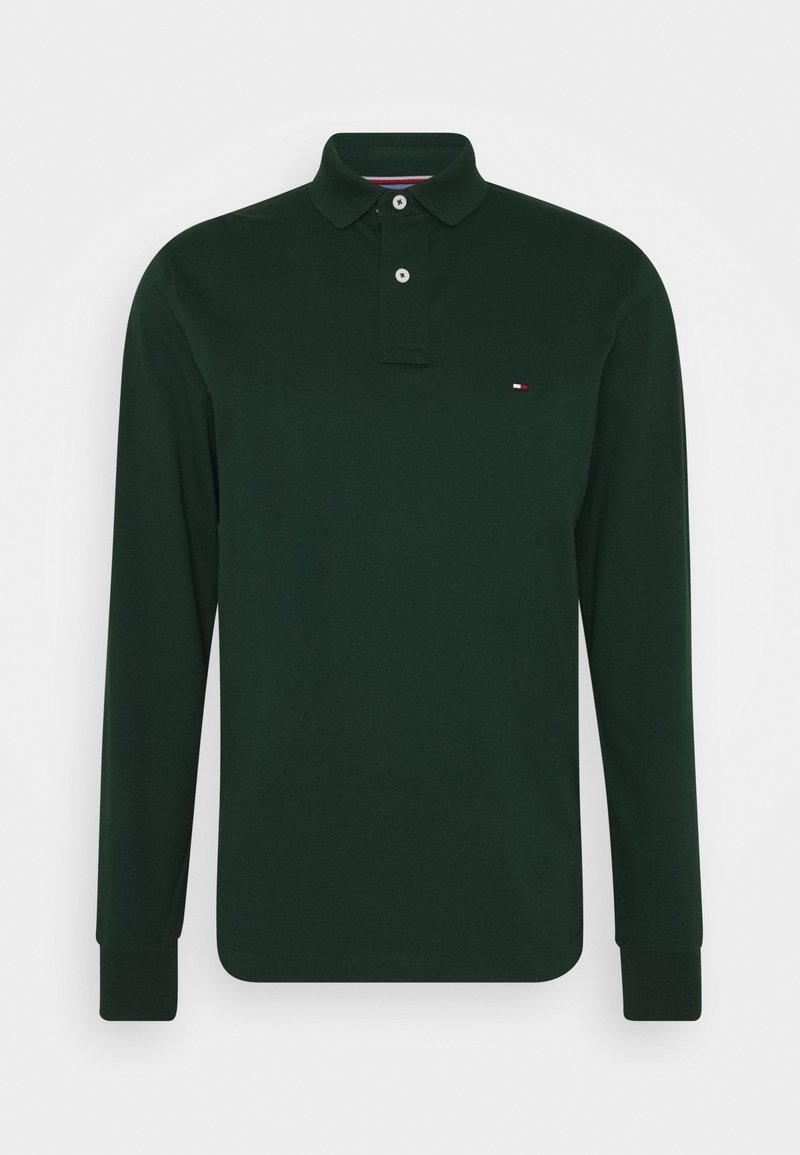 Tmavě zelená polo košile s dlouhým rukávem, se dvěma bílými knoflíky a malým červenobílým modrým vlajkovým logem na levé hrudi.