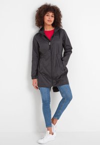 Black lightweight rain jacket with a zip front, two side pockets, and an adjustable hood. Worn over a red top and blue jeans.