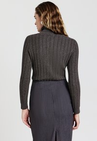 Maglione a costine grigio scuro con colletto alto, caratterizzato da un motivo testurizzato e una silhouette aderente, abbinato a una gonna scura e elegante.