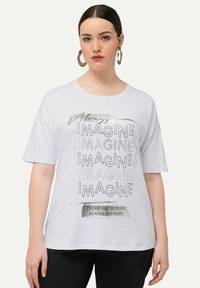 Hvid t-shirt med korte ærmer med sort tekst: "Always IMAGINE" og "DER ER SÅ MANGE GRUNDE TIL AT VÆRE LYKKELIG." Casual pasform, glat tekstur.