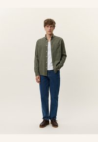 Groene en witte geruite overhemd over een wit T-shirt, gecombineerd met blauwe rechttoe rechtaan jeans en brown schoenen.