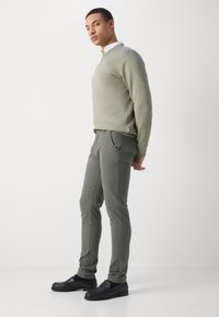 Light gray sweater with a rounded neckline, paired with dark green tailored pants and black loafers, on a plain background.