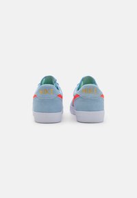 Blaue Wildledersneaker mit einer weißen Gummisohle, versehen mit einem neon-orangenen Akzent und goldener "NIKE"-Branding auf der Ferse.